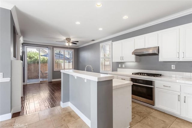 kitchen featuring tile countertops, light hardwood / wood-style flooring, ceiling fan, ornamental molding, and stainless steel appliances