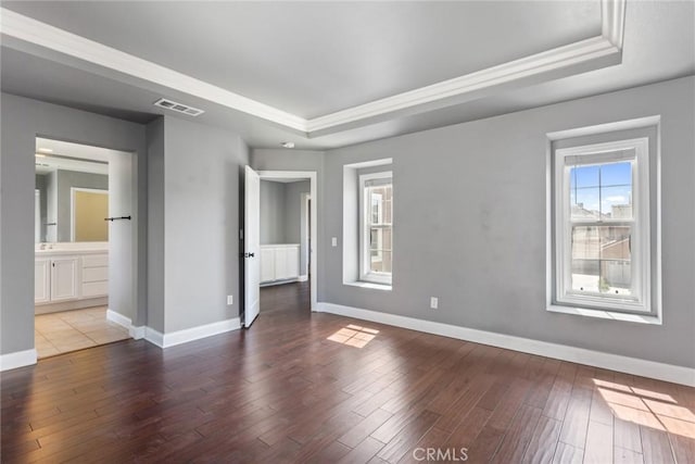 unfurnished bedroom featuring wood-type flooring, a tray ceiling, and ensuite bath