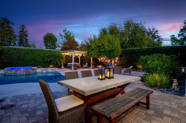 pool at dusk featuring a patio and an in ground hot tub