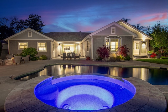 pool at dusk featuring an in ground hot tub and a patio