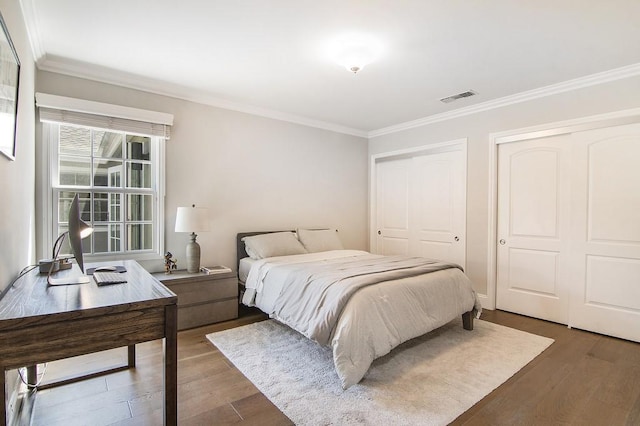 bedroom with visible vents, two closets, wood finished floors, and crown molding