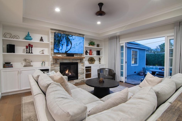 living area featuring built in features, a stone fireplace, wood finished floors, and ornamental molding