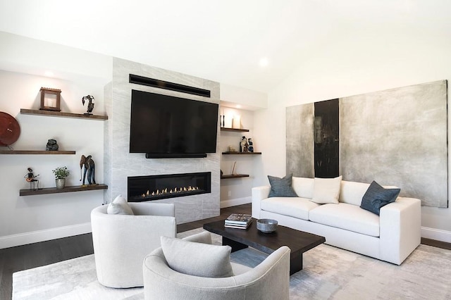 living area featuring baseboards, a large fireplace, lofted ceiling, and wood finished floors