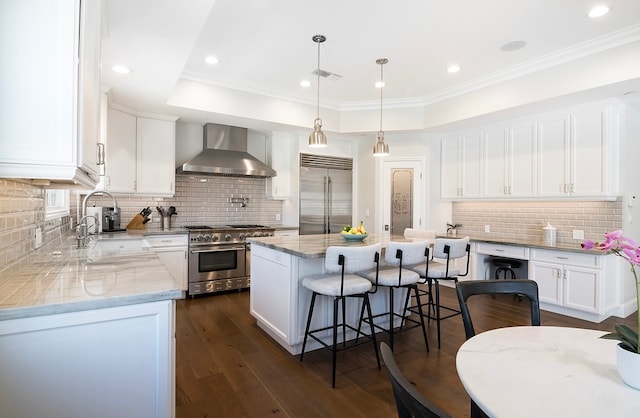 kitchen with high end appliances, white cabinets, and wall chimney range hood