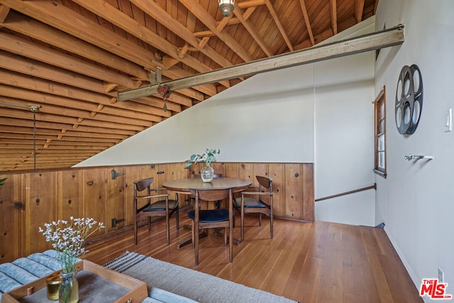 dining space with high vaulted ceiling, wood walls, beamed ceiling, and hardwood / wood-style flooring