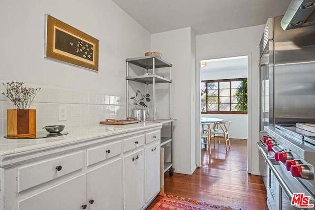 kitchen with decorative backsplash, white cabinets, range hood, and dark wood-type flooring