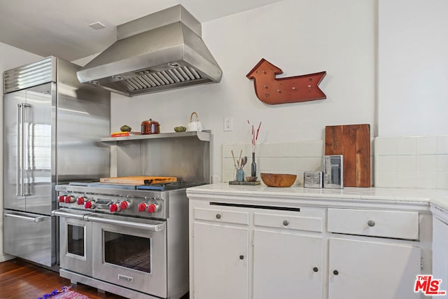 kitchen featuring premium appliances, backsplash, dark wood-type flooring, white cabinetry, and range hood