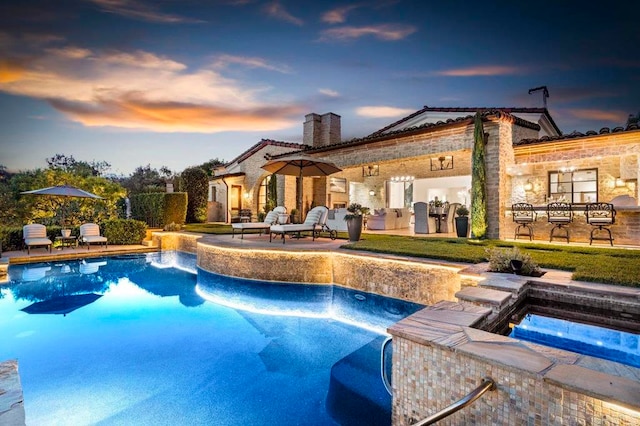 pool at dusk with pool water feature, an in ground hot tub, and a patio area