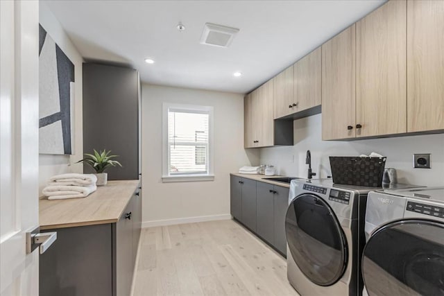 clothes washing area with light hardwood / wood-style flooring, washing machine and dryer, sink, and cabinets