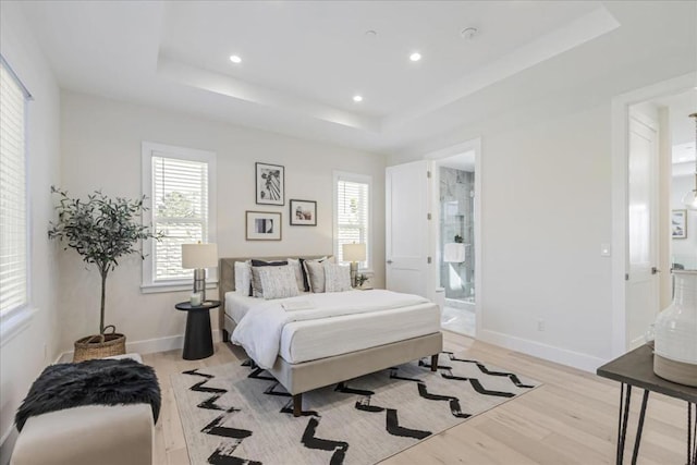 bedroom with light hardwood / wood-style floors, connected bathroom, and a tray ceiling