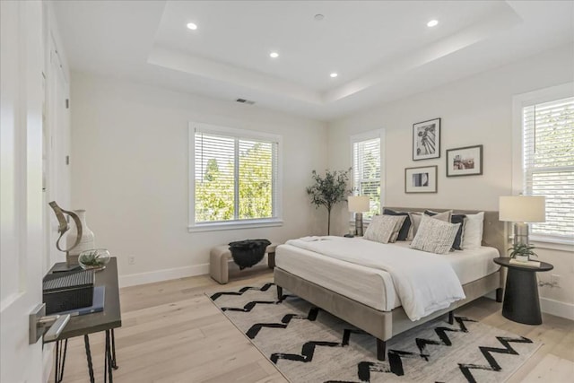 bedroom with a tray ceiling and light hardwood / wood-style flooring