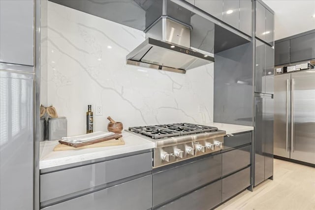 kitchen with light stone countertops, gray cabinets, stainless steel appliances, and range hood