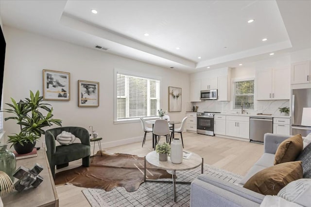 living room featuring light hardwood / wood-style floors, sink, and a tray ceiling