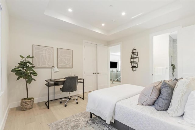 bedroom with ensuite bathroom, light hardwood / wood-style flooring, and a raised ceiling