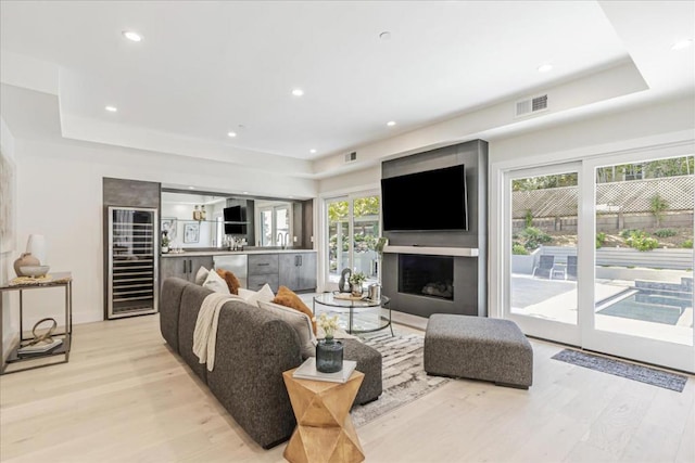 living room featuring a raised ceiling, beverage cooler, and light hardwood / wood-style flooring