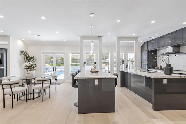 kitchen with wall chimney exhaust hood, pendant lighting, a large island with sink, and a breakfast bar