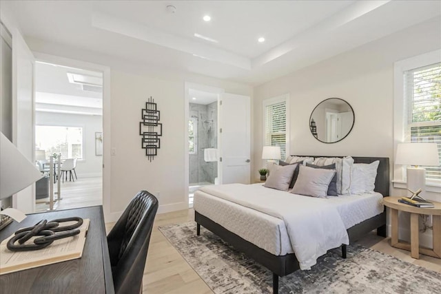 bedroom with a tray ceiling, ensuite bathroom, and light wood-type flooring