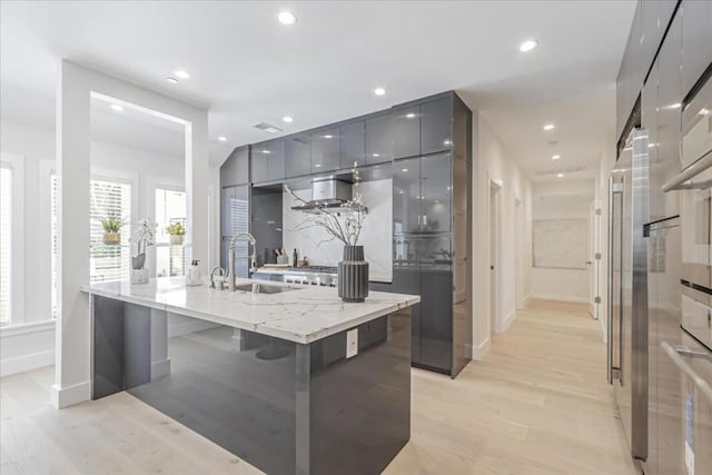 kitchen featuring light hardwood / wood-style floors, sink, light stone counters, a center island with sink, and a breakfast bar area