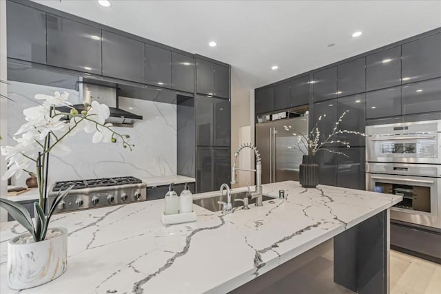 kitchen featuring stainless steel appliances, tasteful backsplash, light wood-type flooring, light stone counters, and sink