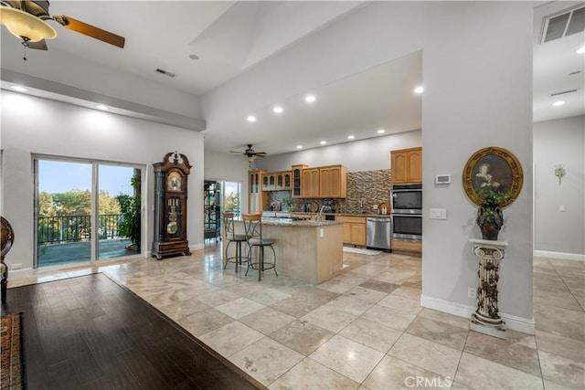kitchen featuring tasteful backsplash, visible vents, a ceiling fan, a high ceiling, and appliances with stainless steel finishes