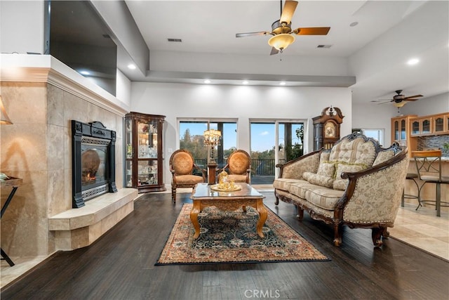 living room featuring hardwood / wood-style floors, a tiled fireplace, a ceiling fan, and a towering ceiling