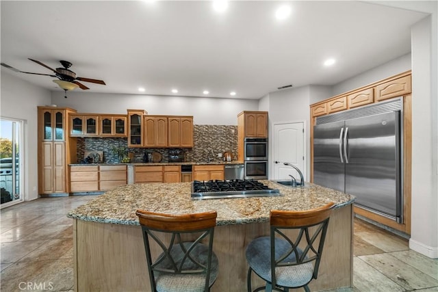 kitchen with a sink, decorative backsplash, a large island, stainless steel appliances, and light stone countertops