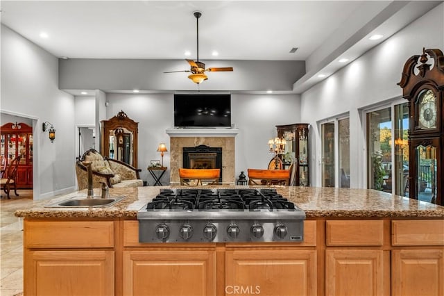 kitchen featuring a sink, stainless steel gas cooktop, ceiling fan, a towering ceiling, and a tiled fireplace
