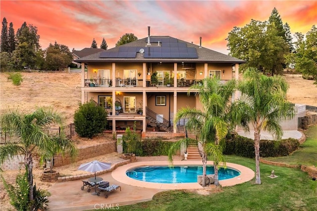 back house at dusk with a fenced in pool, a balcony, a patio, and solar panels