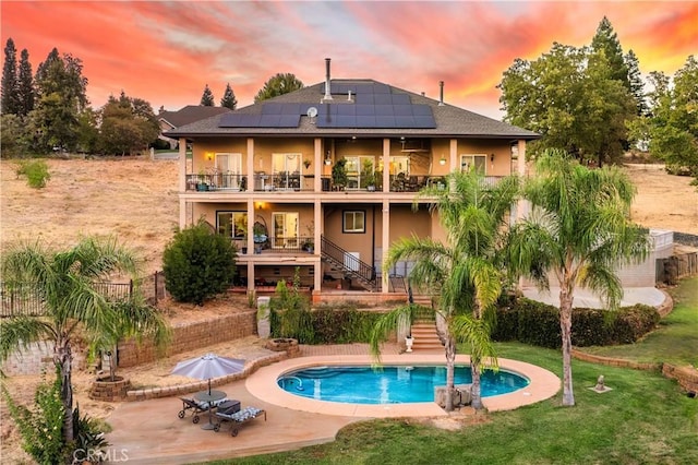 back of property with a fenced in pool, stairs, a yard, solar panels, and a patio area