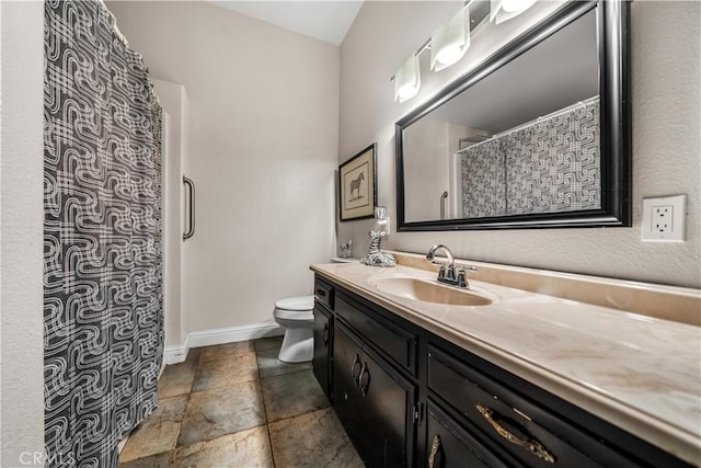 bathroom featuring toilet, vanity, a shower with curtain, stone finish flooring, and baseboards
