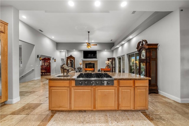 kitchen featuring a center island, a sink, stainless steel gas cooktop, ceiling fan, and a fireplace