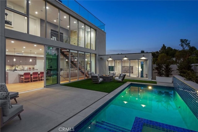 back house at dusk with a patio area, a fenced in pool, and sink