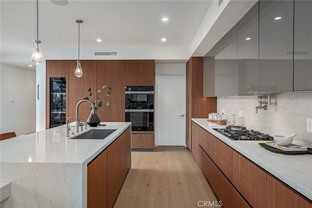 kitchen with a spacious island, sink, black double oven, gas stovetop, and decorative light fixtures