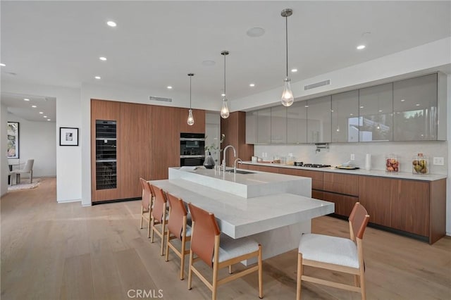 kitchen featuring sink, a large island with sink, light hardwood / wood-style floors, decorative light fixtures, and a breakfast bar area