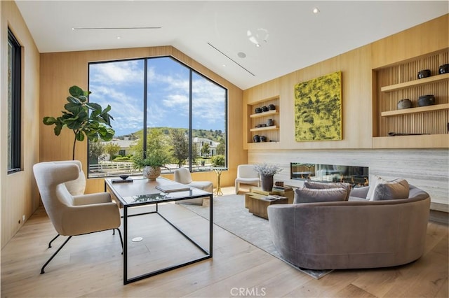 living room with wooden walls, built in features, lofted ceiling, and light wood-type flooring