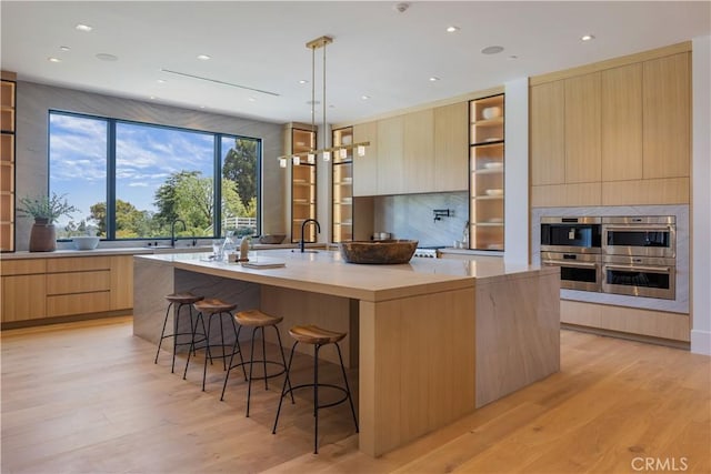 kitchen featuring light brown cabinets, hanging light fixtures, a kitchen breakfast bar, light hardwood / wood-style floors, and a kitchen island with sink