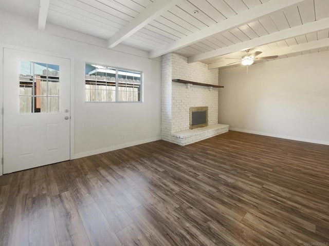 unfurnished living room featuring dark wood-type flooring, a brick fireplace, ceiling fan, beamed ceiling, and wood ceiling