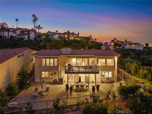 back house at dusk featuring a balcony, a patio, and central air condition unit