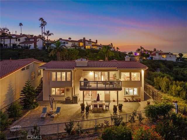 back of house featuring a balcony, a patio, stucco siding, a fenced backyard, and a chimney