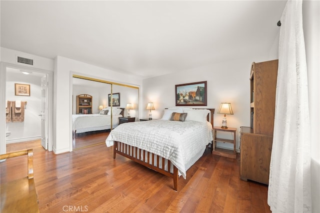 bedroom with a closet, ensuite bathroom, visible vents, and wood finished floors