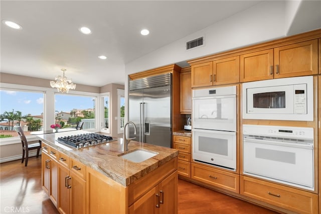 kitchen featuring sink, a center island with sink, a chandelier, built in appliances, and dark hardwood / wood-style flooring