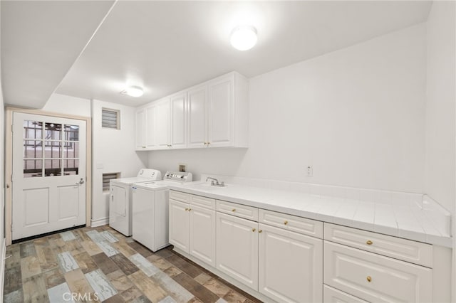 clothes washing area featuring cabinet space, washing machine and dryer, light wood-style flooring, and a sink