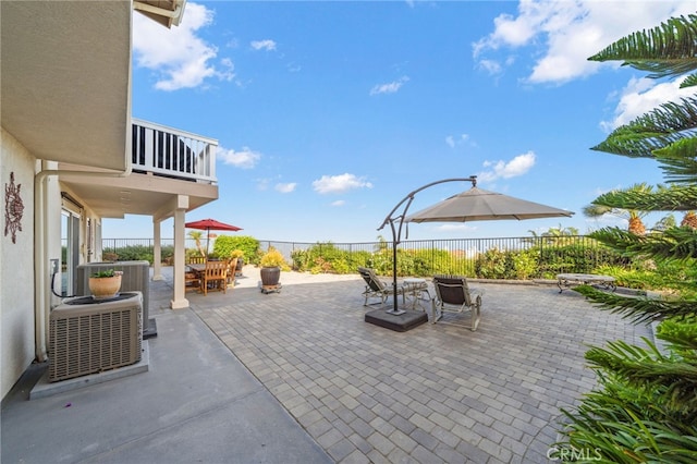 view of patio with fence, outdoor dining area, central AC, and a balcony