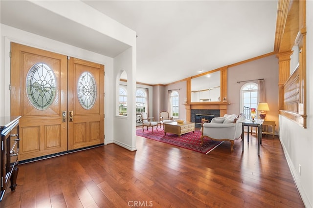 entrance foyer with dark wood finished floors, baseboards, ornamental molding, and a glass covered fireplace