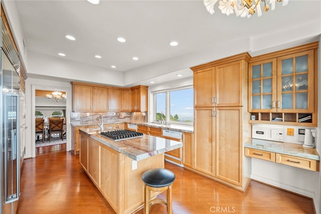 kitchen featuring tasteful backsplash, light stone countertops, a center island, light hardwood / wood-style flooring, and a chandelier