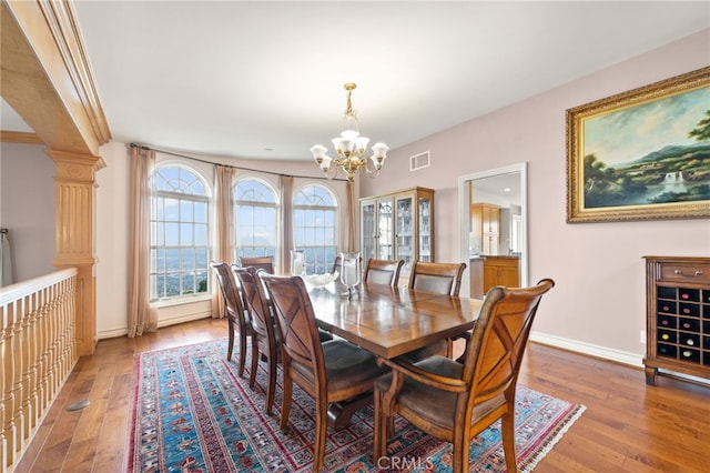 dining space with wood-type flooring, an inviting chandelier, and decorative columns