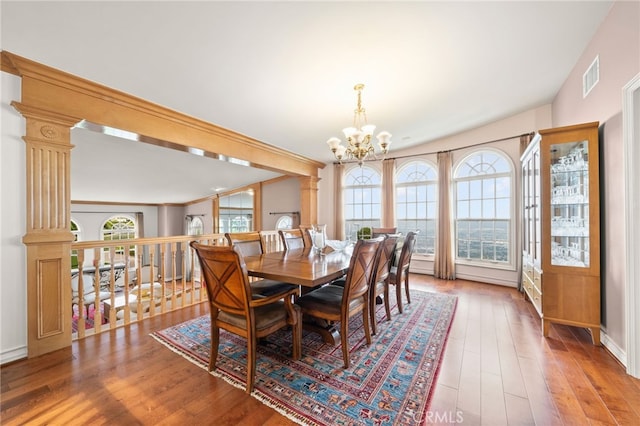 dining space featuring wood-type flooring, ornamental molding, an inviting chandelier, and ornate columns