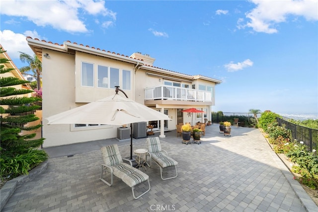 rear view of house with a balcony, fence, a patio, central air condition unit, and stucco siding