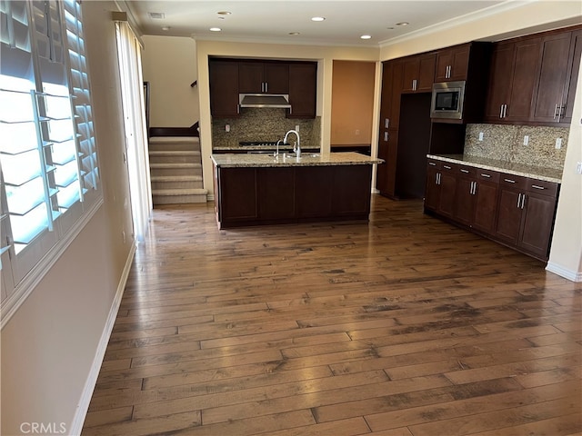 kitchen featuring backsplash, stainless steel microwave, and dark wood-type flooring