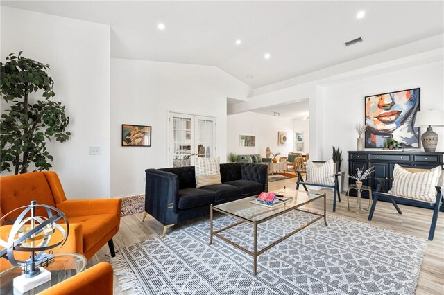 living room with french doors, light hardwood / wood-style floors, and lofted ceiling